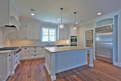 Example of a large classic u-shaped medium tone wood floor enclosed kitchen design in Portland with an undermount sink, shaker cabinets, white cabinets, granite countertops, white backsplash, ceramic backsplash, stainless steel appliances and an island
