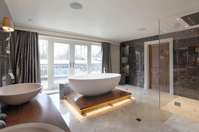 This is an example of a contemporary bathroom in Cheshire with recessed-panel cabinets, dark wood cabinets, wood benchtops, a freestanding tub, beige tile and marble floors.