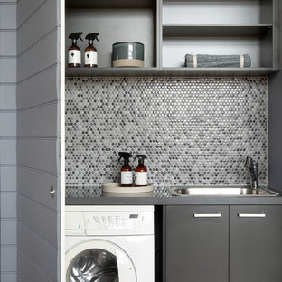 メルボルンの小さいコンテンポラリースタイルのおしゃれな洗濯室 (シングルシンク、フラットパネル扉のキャビネット、グレーのキャビネット、クオーツストーンカウンター、グレーの壁、無垢フローリング、目隠し付き洗濯機・乾燥機、茶色い床、グレーのキッチンカウンター) の写真