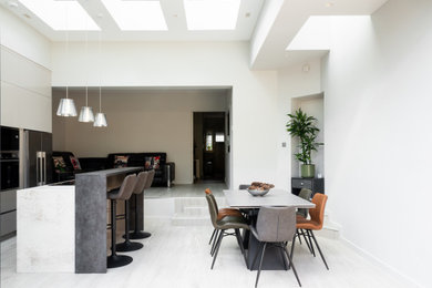 Large contemporary kitchen/dining room in London with white walls, light hardwood flooring, grey floors, a vaulted ceiling and feature lighting.