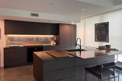 Example of a mid-sized trendy concrete floor and gray floor eat-in kitchen design in Cedar Rapids with an undermount sink, flat-panel cabinets, black cabinets, granite countertops, metallic backsplash, glass sheet backsplash, an island and gray countertops