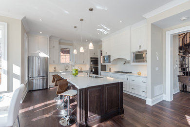 Large transitional l-shaped dark wood floor and brown floor eat-in kitchen photo in Toronto with an undermount sink, stainless steel appliances, recessed-panel cabinets, white cabinets, solid surface countertops, white backsplash, subway tile backsplash, an island and white countertops