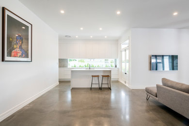 This is an example of a large contemporary kitchen in Brisbane with flat-panel cabinets, white cabinets, stainless steel appliances, concrete floors, with island, grey floor and white benchtop.