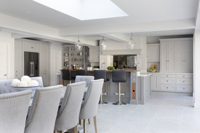 Design ideas for a large classic grey and white l-shaped open plan kitchen in Surrey with a built-in sink, shaker cabinets, grey cabinets, quartz worktops, metallic splashback, mirror splashback, stainless steel appliances, limestone flooring, an island, grey floors, white worktops and exposed beams.
