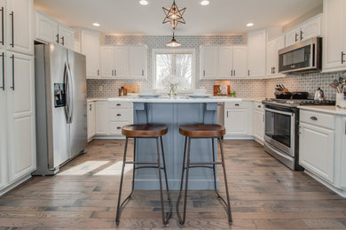 Example of a classic u-shaped dark wood floor and brown floor kitchen design in Grand Rapids with raised-panel cabinets, white cabinets, stainless steel appliances, an island and white countertops