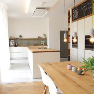 Design ideas for a large scandinavian galley open plan kitchen in Dortmund with a drop-in sink, flat-panel cabinets, white cabinets, wood benchtops, green splashback, subway tile splashback, stainless steel appliances, concrete floors, with island and grey floor.
