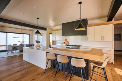 Large trendy single-wall medium tone wood floor and brown floor kitchen photo in Denver with an undermount sink, flat-panel cabinets, white cabinets, quartz countertops, white backsplash, quartz backsplash, paneled appliances, two islands and white countertops