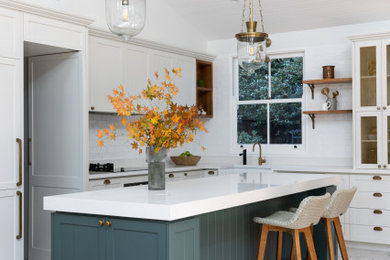 Réalisation d'une cuisine ouverte bohème en L de taille moyenne avec un évier de ferme, un placard à porte shaker, des portes de placard grises, un plan de travail en quartz modifié, une crédence blanche, une crédence en céramique, un électroménager noir, un sol en carrelage de porcelaine, îlot, un sol blanc, un plan de travail blanc et poutres apparentes.