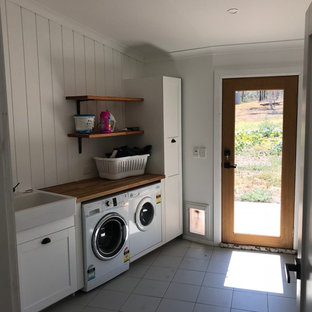 Design ideas for a mid-sized modern single-wall dedicated laundry room in Central Coast with an utility sink, recessed-panel cabinets, white cabinets, wood benchtops, white walls, ceramic floors, a side-by-side washer and dryer, grey floor and brown benchtop.