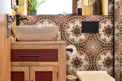 Inspiration for a small mediterranean ensuite bathroom in Manchester with shaker cabinets, light wood cabinets, a wall mounted toilet, multi-coloured tiles, cement tiles, yellow walls, cement flooring, wooden worktops, multi-coloured floors, a single sink, a freestanding vanity unit, a vessel sink and beige worktops.