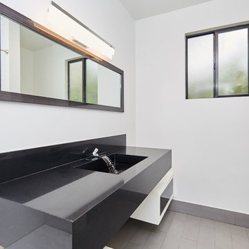 Black Stone Vanity With Running Water and Toilet Beyond