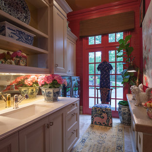 アトランタの中サイズのトラディショナルスタイルのおしゃれな家事室 (白いキャビネット、クオーツストーンカウンター、左右配置の洗濯機・乾燥機、アンダーカウンターシンク、赤い壁、ライムストーンの床、落し込みパネル扉のキャビネット) の写真