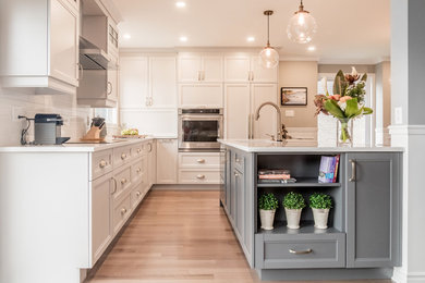 Example of a mid-sized transitional l-shaped medium tone wood floor and brown floor eat-in kitchen design in Montreal with an undermount sink, recessed-panel cabinets, white cabinets, quartz countertops, white backsplash, ceramic backsplash, paneled appliances and an island