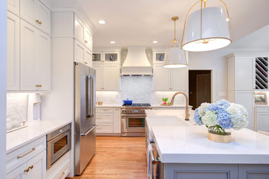 Mid-sized elegant l-shaped medium tone wood floor and brown floor eat-in kitchen photo in Raleigh with a farmhouse sink, recessed-panel cabinets, white cabinets, quartz countertops, white backsplash, marble backsplash, stainless steel appliances, an island and white countertops
