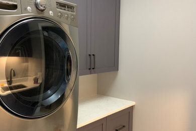 Example of a mid-sized trendy single-wall porcelain tile and multicolored floor dedicated laundry room design in Orlando with an undermount sink, shaker cabinets, gray cabinets, quartz countertops, white backsplash, quartz backsplash, gray walls, a stacked washer/dryer and white countertops