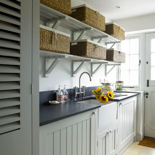 Inspiration for a country utility room in Wiltshire with a belfast sink, shaker cabinets, granite worktops, travertine flooring and a concealed washer and dryer.