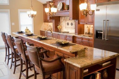 Large elegant l-shaped travertine floor eat-in kitchen photo in Philadelphia with an undermount sink, raised-panel cabinets, medium tone wood cabinets, granite countertops, beige backsplash, stone tile backsplash, stainless steel appliances and an island