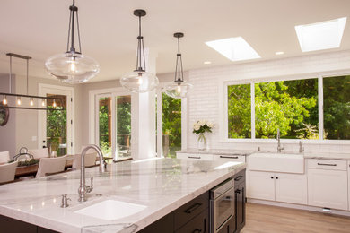 Large elegant u-shaped light wood floor and brown floor eat-in kitchen photo in Seattle with a farmhouse sink, shaker cabinets, white cabinets, granite countertops, white backsplash, subway tile backsplash, stainless steel appliances, an island and white countertops
