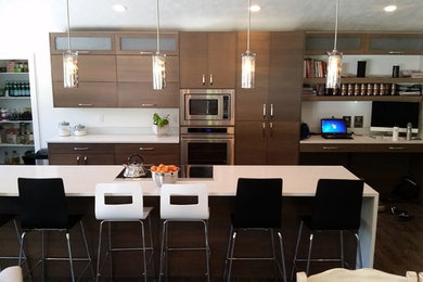 Example of a mid-sized trendy l-shaped dark wood floor eat-in kitchen design in Orange County with a drop-in sink, flat-panel cabinets, dark wood cabinets, solid surface countertops, white backsplash, stone slab backsplash, stainless steel appliances and an island