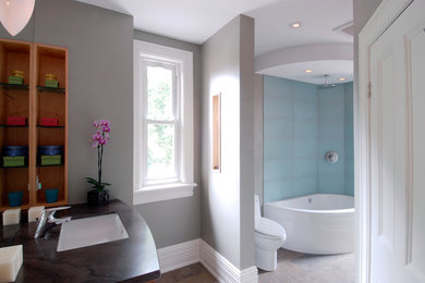 This is an example of a contemporary bathroom in Ottawa with an undermount sink, flat-panel cabinets, medium wood cabinets, granite benchtops, a corner tub, a corner shower, a one-piece toilet, blue tile and glass tile.