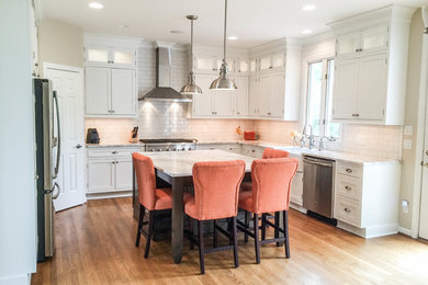 This is an example of a mid-sized transitional u-shaped eat-in kitchen in Cincinnati with a farmhouse sink, recessed-panel cabinets, white cabinets, quartzite benchtops, white splashback, subway tile splashback, stainless steel appliances, light hardwood floors and with island.