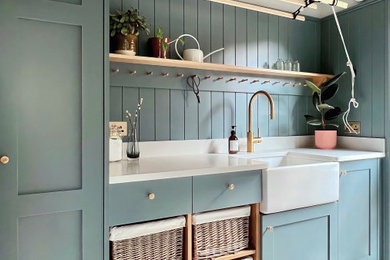 This is an example of a small traditional utility room in Other with a belfast sink, shaker cabinets, blue cabinets, quartz worktops, blue walls, porcelain flooring, a stacked washer and dryer, white worktops and tongue and groove walls.