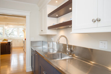 Example of a mid-sized beach style single-wall light wood floor and beige floor home bar design in Providence with an integrated sink, shaker cabinets, white cabinets and stainless steel countertops