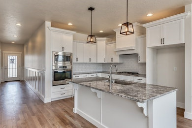 Example of a mid-sized trendy single-wall medium tone wood floor open concept kitchen design in Boise with an undermount sink, flat-panel cabinets, white cabinets, granite countertops, white backsplash, porcelain backsplash, stainless steel appliances and an island