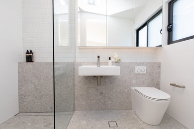This is an example of a small contemporary master bathroom in Sydney with a curbless shower, white tile, matchstick tile, porcelain floors, a wall-mount sink, grey floor, an open shower, a niche, a single vanity and vaulted.