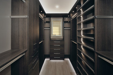 This is an example of a mid-sized arts and crafts men's walk-in wardrobe in Orange County with flat-panel cabinets, grey cabinets, light hardwood floors and beige floor.