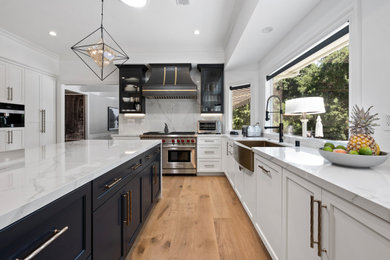 Inspiration for a light wood floor and beige floor kitchen remodel in Los Angeles with a farmhouse sink, shaker cabinets, white cabinets, quartz countertops, quartz backsplash, stainless steel appliances, an island and white countertops