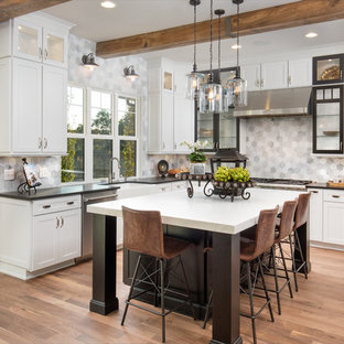 コロンバスのカントリー風おしゃれなキッチン (エプロンフロントシンク、シェーカースタイル扉のキャビネット、白いキャビネット、グレーのキッチンパネル、シルバーの調理設備の、無垢フローリング、茶色い床、黒いキッチンカウンター) の写真