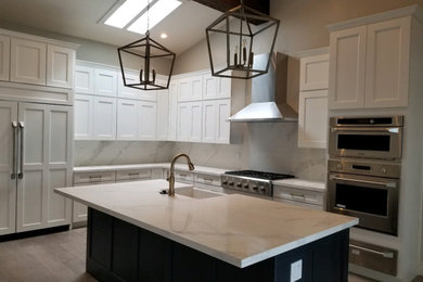 Design ideas for a mid-sized transitional l-shaped eat-in kitchen in Sacramento with a farmhouse sink, shaker cabinets, white cabinets, stainless steel appliances, laminate floors, with island, brown floor, quartz benchtops, white splashback, stone slab splashback and white benchtop.