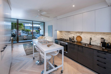 This is an example of a mid-sized contemporary single-wall open plan kitchen in Sydney with an undermount sink, flat-panel cabinets, white cabinets, white splashback, stainless steel appliances, light hardwood floors, with island, marble benchtops and marble splashback.