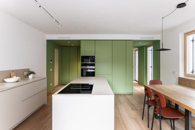 This is an example of a small modern open plan kitchen in Other with a submerged sink, flat-panel cabinets, green cabinets, composite countertops, beige splashback, black appliances, light hardwood flooring, an island, beige worktops and a drop ceiling.