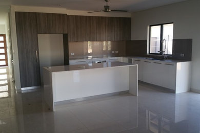 Photo of a mid-sized modern l-shaped open plan kitchen in Darwin with an undermount sink, flat-panel cabinets, white cabinets, quartz benchtops, brown splashback, glass sheet splashback, stainless steel appliances, porcelain floors and with island.