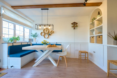 Inspiration for a medium sized modern dining room with banquette seating, white walls, laminate floors, brown floors, exposed beams and feature lighting.
