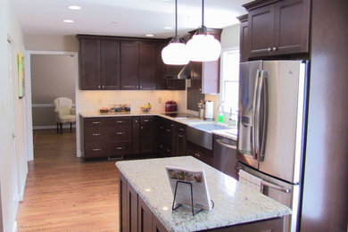 Mid-sized trendy l-shaped medium tone wood floor and brown floor enclosed kitchen photo in DC Metro with a farmhouse sink, recessed-panel cabinets, brown cabinets, granite countertops, white backsplash, stainless steel appliances, an island and beige countertops