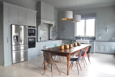 Geräumige Country Wohnküche ohne Insel in L-Form mit Landhausspüle, Küchenrückwand in Blau, schwarzen Elektrogeräten, hellem Holzboden, Schrankfronten im Shaker-Stil und blauen Schränken in Berlin