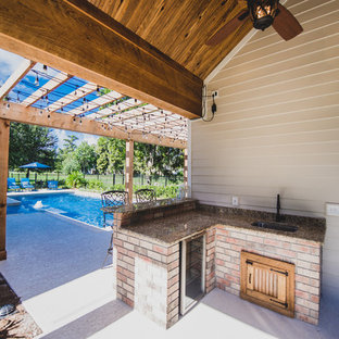 ニューオリンズの小さいトラディショナルスタイルのおしゃれな着席型バー (御影石カウンター、アンダーカウンターシンク、ルーバー扉のキャビネット、中間色木目調キャビネット、ベージュキッチンパネル、石スラブのキッチンパネル、コンクリートの床) の写真