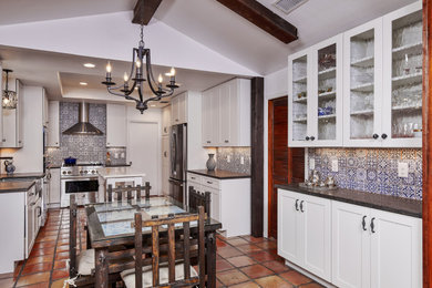 Example of a mid-sized southwest galley terra-cotta tile, red floor and tray ceiling eat-in kitchen design in Other with a farmhouse sink, shaker cabinets, white cabinets, granite countertops, blue backsplash, terra-cotta backsplash, stainless steel appliances, an island and brown countertops