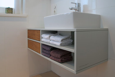 Imagen de aseo moderno pequeño con armarios con paneles lisos, puertas de armario de madera clara y baldosas y/o azulejos blancos