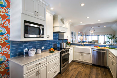 Photo of a mid-sized beach style u-shaped kitchen in Miami with a farmhouse sink, raised-panel cabinets, white cabinets, quartz benchtops, blue splashback, porcelain splashback, stainless steel appliances, porcelain floors and brown floor.