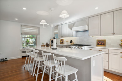 Mid-sized galley light wood floor and brown floor eat-in kitchen photo in Philadelphia with a drop-in sink, flat-panel cabinets, white cabinets, quartz countertops, white backsplash, ceramic backsplash, stainless steel appliances, an island and white countertops