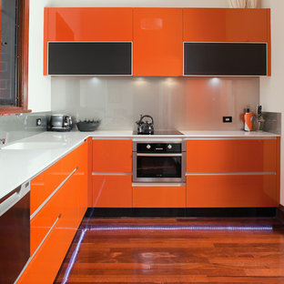Cette photo montre une arrière-cuisine tendance en L de taille moyenne avec un évier intégré, un placard à porte plane, des portes de placard oranges, un plan de travail en surface solide, une crédence métallisée, une crédence en feuille de verre, un électroménager en acier inoxydable, un sol en bois foncé et aucun îlot.