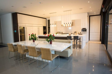 Inspiration for a large modern galley marble floor eat-in kitchen remodel in Toronto with a single-bowl sink, flat-panel cabinets, white cabinets, solid surface countertops, white backsplash, stone slab backsplash, stainless steel appliances and an island