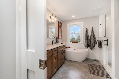 Bathroom - mid-sized transitional master white tile and porcelain tile porcelain tile, gray floor and double-sink bathroom idea in Baltimore with recessed-panel cabinets, brown cabinets, a one-piece toilet, white walls, an undermount sink, quartz countertops, a hinged shower door, beige countertops and a built-in vanity