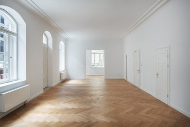 Großes Klassisches Arbeitszimmer mit Arbeitsplatz, weißer Wandfarbe, hellem Holzboden, freistehendem Schreibtisch und braunem Boden in München