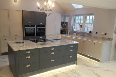 Inspiration for a large classic grey and white l-shaped open plan kitchen in Essex with a single-bowl sink, flat-panel cabinets, grey cabinets, granite worktops, grey splashback, granite splashback, black appliances, porcelain flooring, an island, white floors and grey worktops.