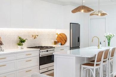 This is an example of a mid-sized beach style galley open plan kitchen in Sydney with an undermount sink, shaker cabinets, white cabinets, recycled glass benchtops, white splashback, ceramic splashback, medium hardwood floors, with island and white benchtop.